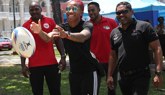 Commonwealth Games 100 metres gold mnedallist T&T’s Michelle-Lee Ahye, centre, tries her hand at rugby during the T&T Olympic Committee’s observance of International Olympic Day at Woodford Square, Port-of-Spain, back in June.  CA-images/ Allan Crane
